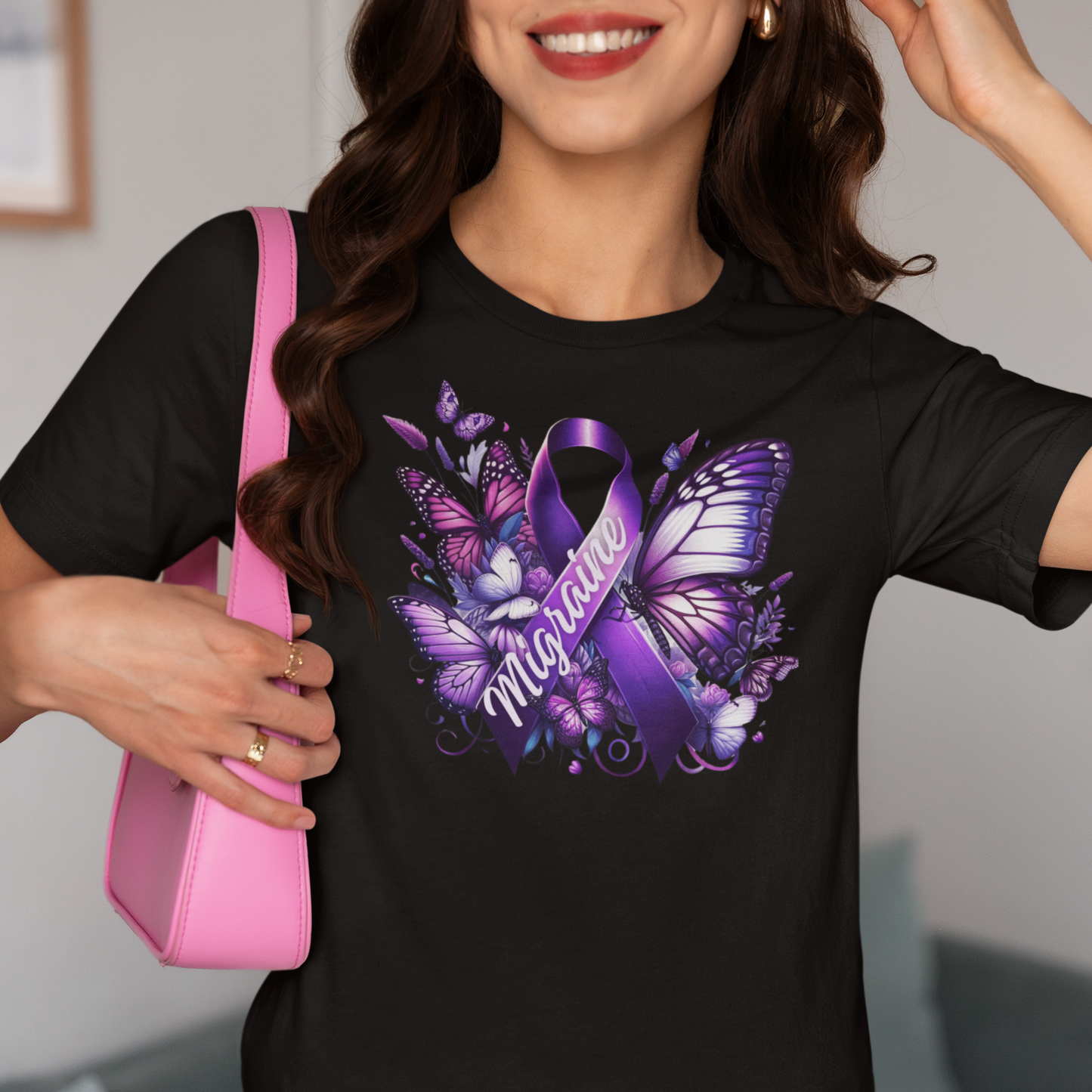 Woman with dark hair and red lipstick carrying a pink purse is wearing a black Migraine Awareness t-shirt with a purple Migraine ribbon and butterflies and flowers